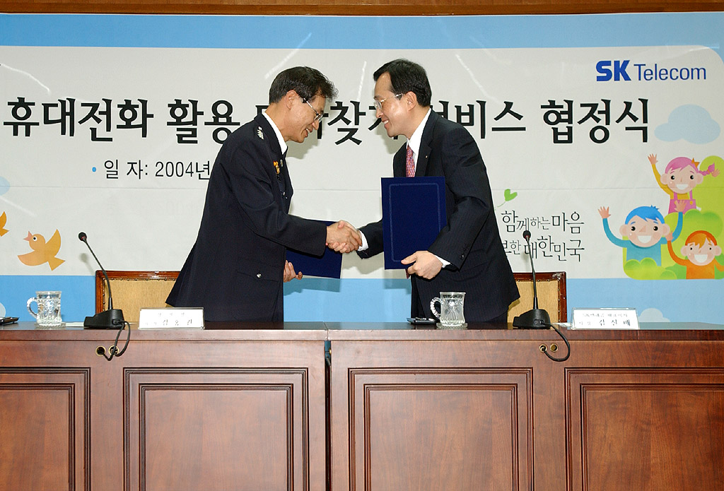 Hong Kweon Kim, vice-deputy director of the Korean National Police Agency (center), and Shin Bae Kim, president of SK Telecom, are shown signing the agreement for the Missing Child Finding Service Using Cellular Phones, and later observing a trial of the service performance. (A recovery of lost children service through the use of cellular Phones was activated on the third of May in a cooperative effort between SK Telecom and the Korean National Police Agency.)